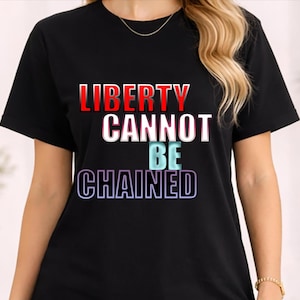 Puede incluir: Camiseta negra con la frase "LIBERTY CANNOT BE CHAINED" en letras rojas, blancas, azules y moradas. La camiseta de manga corta tiene cuello redondo y el texto está centrado. Una prenda informal para el día a día.