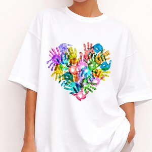 Op de afbeelding: Wit T-shirt met een hartvormig ontwerp gemaakt van kleurrijke handafdrukken. De handafdrukken zijn in tinten blauw, groen, geel, roze, paars en oranje. Het shirt heeft een relaxte pasvorm en korte mouwen.