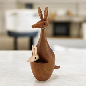 May include: A wooden kangaroo figurine with a joey in its pouch. The kangaroo is brown and the joey is light brown. The figurine is made of wood and has a smooth finish.