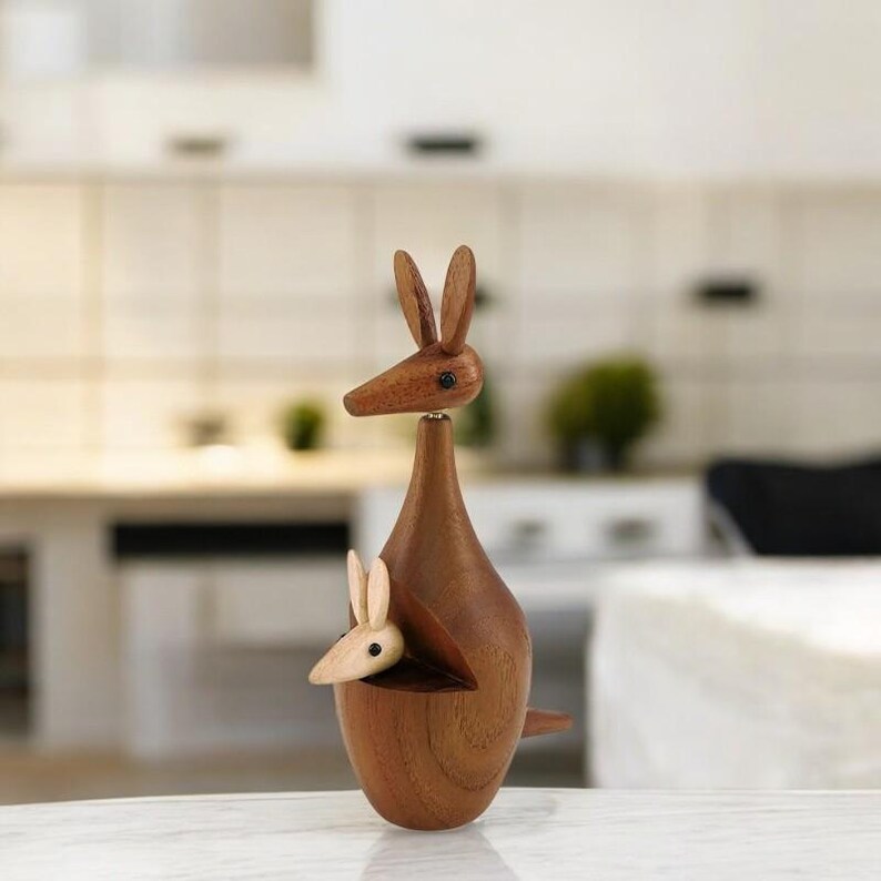 May include: A wooden kangaroo figurine with a joey in its pouch. The kangaroo is brown and the joey is light brown. The figurine is made of wood and has a smooth finish.