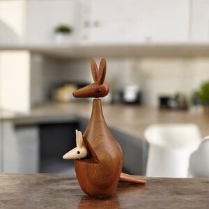 May include: A wooden kangaroo figurine with a joey in its pouch. The kangaroo is brown and the joey is light brown. The figurine is made of wood and has a smooth finish.