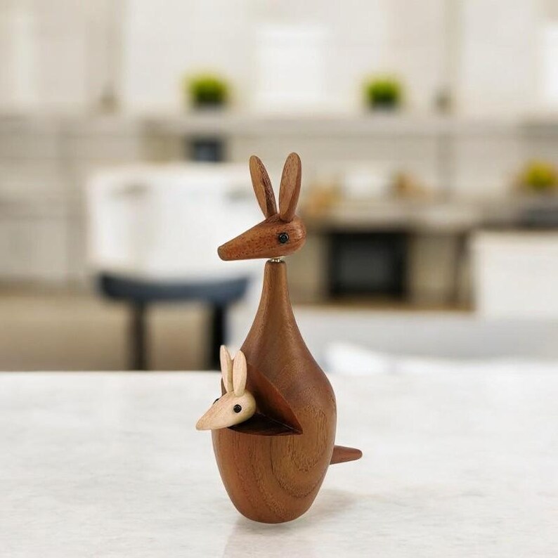 May include: A wooden kangaroo figurine with a joey in its pouch. The kangaroo is brown and the joey is light brown. The figurine is made of wood and has a smooth finish.
