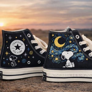 Puede incluir: Zapatillas Converse altas negras con bordado personalizado. Una zapatilla presenta el logo Converse All Star y Snoopy. La otra tiene un diseño de noche estrellada con Snoopy. El texto "SBONGSTITCHDESIGNS" está en la suela.