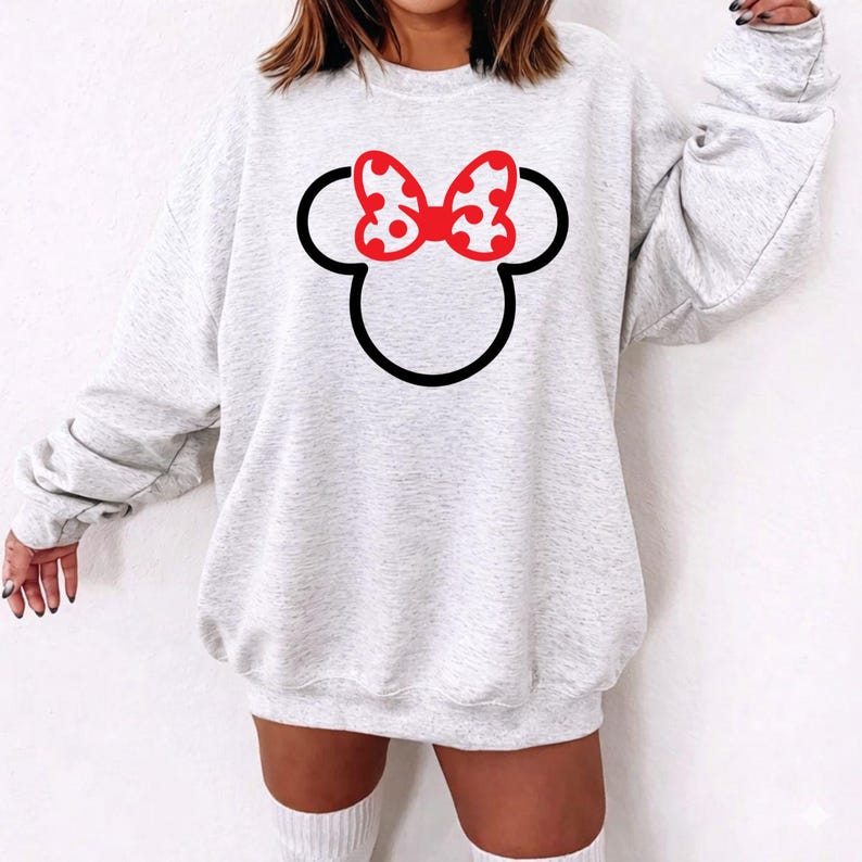 Puede incluir: Una sudadera gris claro con un contorno negro de la cabeza de Mickey Mouse y un lazo rojo con lunares. La sudadera es de estilo casual, adecuada para el uso diario.
