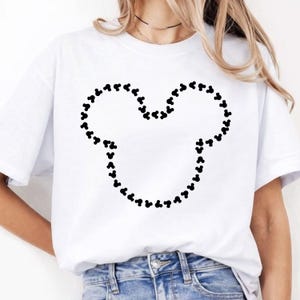 Puede incluir: Camiseta blanca con un contorno de cabeza de Mickey Mouse negro hecho de peque&ntilde;as siluetas de Mickey Mouse. La camiseta es de cuello redondo y est&aacute; hecha de un material suave y c&oacute;modo.