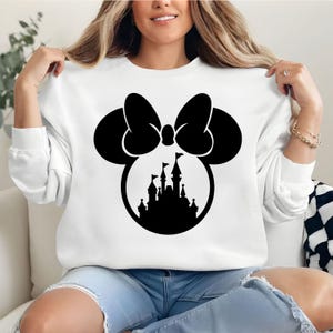 Puede incluir: Sudadera blanca con un dise&ntilde;o negro de Minnie Mouse, que incluye un lazo y una silueta de castillo. El gr&aacute;fico est&aacute; centrado en la parte delantera de la parte superior de manga larga. La sudadera es de material suave.
