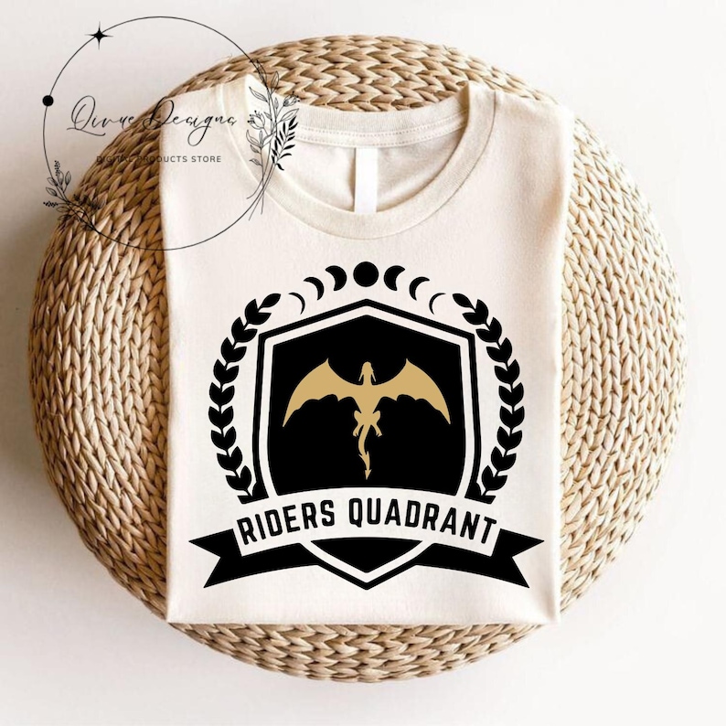 May include: A white t-shirt with a black and gold design. The design features a shield with a dragon inside, a laurel wreath, and the text "Riders Quadrant".