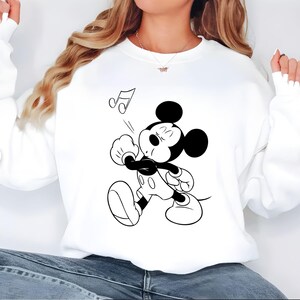 Puede incluir: Sudadera blanca con una ilustraci&oacute;n en blanco y negro de Mickey Mouse cantando. Mickey tiene los ojos cerrados y una nota musical sobre su cabeza. La sudadera es de estilo casual.