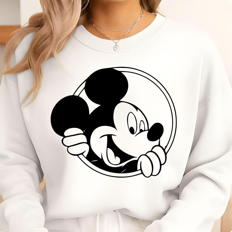 Puede incluir: Sudadera blanca con un gr&aacute;fico en blanco y negro de Mickey Mouse dentro de un c&iacute;rculo. El personaje de dibujos animados est&aacute; sonriendo. La sudadera tiene cuello redondo y mangas largas.