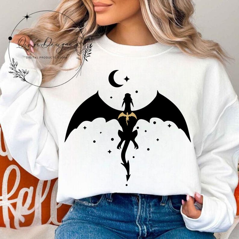 May include: White sweatshirt with a black silhouette of a dragon flying in front of a crescent moon and stars.