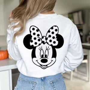 Puede incluir: Sudadera blanca de manga larga con un dise&ntilde;o de Minnie Mouse en blanco y negro en la espalda. El dise&ntilde;o incluye la cara de Minnie, un lazo de lunares y sus ic&oacute;nicas orejas. La sudadera es de material suave.