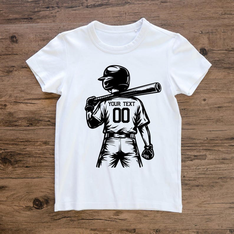 May include: White t-shirt featuring a black and white illustration of a baseball player holding a bat. The player wears a helmet and the shirt displays "YOUR TEXT" above the number "00". The design is a graphic representation of a baseball theme.