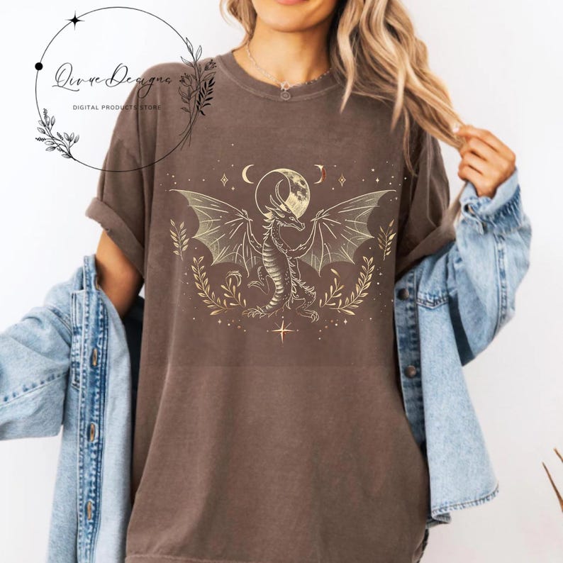 May include: A brown t-shirt with a gold graphic of a dragon standing in front of a full moon. The dragon has wings spread out and is surrounded by stars and crescent moons.