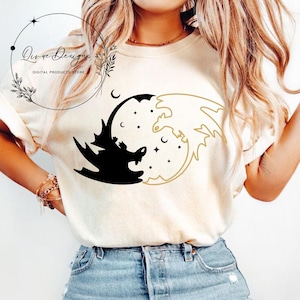 May include: A white t-shirt with a black and white yin yang design featuring two dragons. The dragons are facing each other, with one dragon being black and the other white. The design is surrounded by a circle of stars.