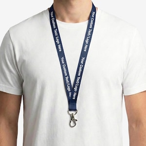 Puede incluir: Cordón azul marino con el texto "Your Custom Text/Logo Here" impreso en blanco. Tiene un cierre de metal y se lleva alrededor del cuello de una persona. La persona lleva una camiseta blanca. El cordón es un artículo promocional.