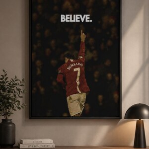 May include: A framed wall art print featuring a soccer player from behind, wearing a red jersey with the name RONALDO and the number 7 on the back. The player has one arm raised, and the word BELIEVE is printed in white above the figure.