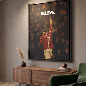 May include: A framed rectangular wall art print featuring a soccer player wearing a red jersey with the name RONALDO and the number 7 on the back, pointing a finger upward. The word BELIEVE is printed in white capital letters above the player.