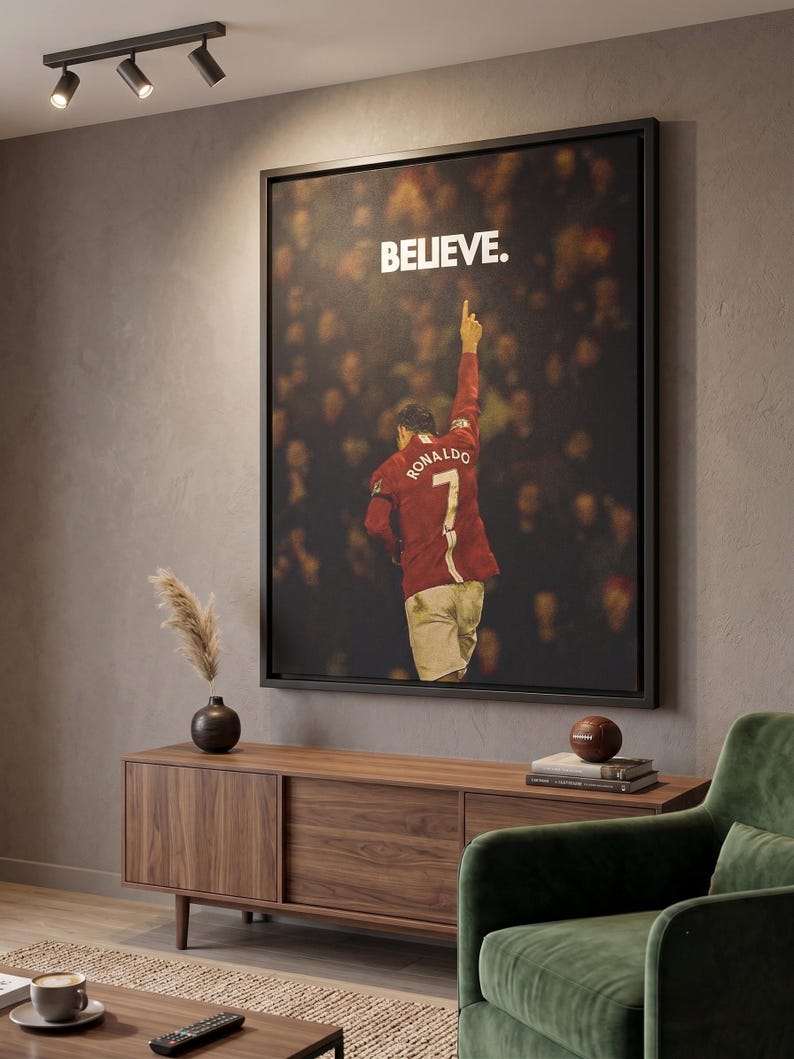 May include: A framed rectangular wall art print featuring a soccer player wearing a red jersey with the name RONALDO and the number 7 on the back, pointing a finger upward. The word BELIEVE is printed in white capital letters above the player.