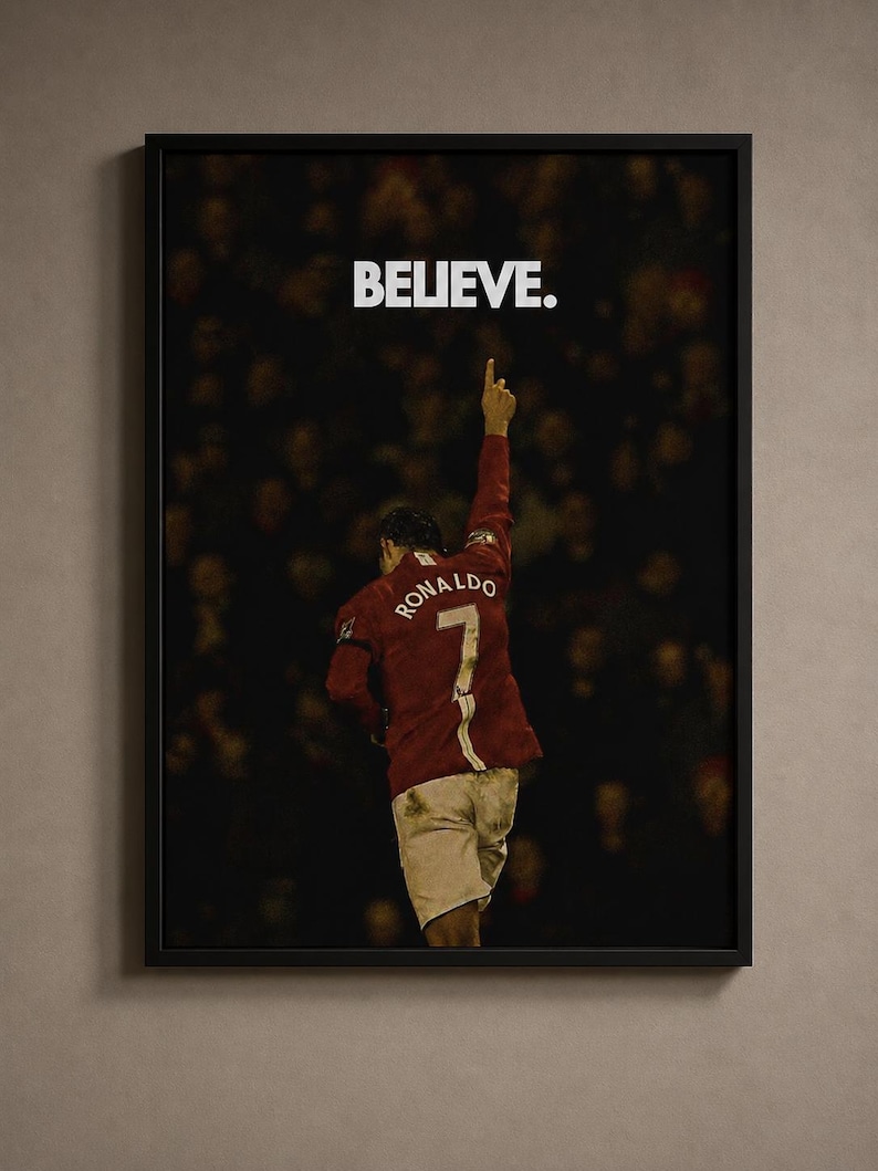 May include: A framed wall poster featuring a soccer player from behind, wearing a red jersey with the name RONALDO and the number 7 on the back. The player has one arm raised toward the sky. Above the player, the word BELIEVE is printed in white.