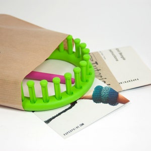 May include: A green plastic knitting loom with a pink knitting needle, a brown paper envelope, and a printed instruction sheet with the text "Tutorials" and "Paperpine.com".