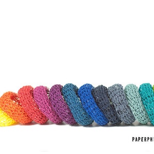 Könnte beinhalten: Eine Reihe bunter gehäkelter Ringe in einem Regenbogen-Farbverlauf, beginnend mit Gelb und endend mit Grün. Die Ringe sind aus einem feinen, zarten Garn gefertigt und haben eine leicht strukturierte Oberfläche.