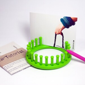 May include: Green knitting loom with 20 pegs, a pink crochet hook, and a printed instruction sheet that says "Knit Bangles Instructions Tutorial".