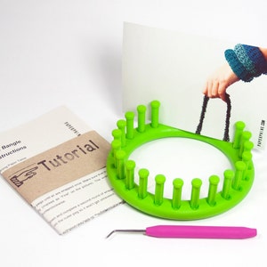 Könnte beinhalten: Grüne Stricknadel mit 20 Stiften, einem rosa Häkelhaken und einer braunen Papier-Anleitung mit dem Text "Knit Bangle Instructions" und "Tutorial".