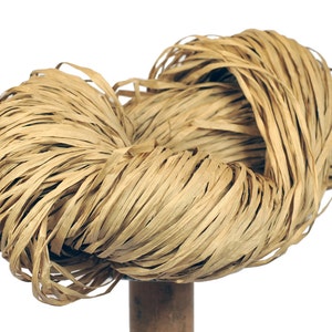 May include: A bundle of natural raffia fiber, a light brown color, in a loose, tangled knot. The raffia is made of thin, woven strands.