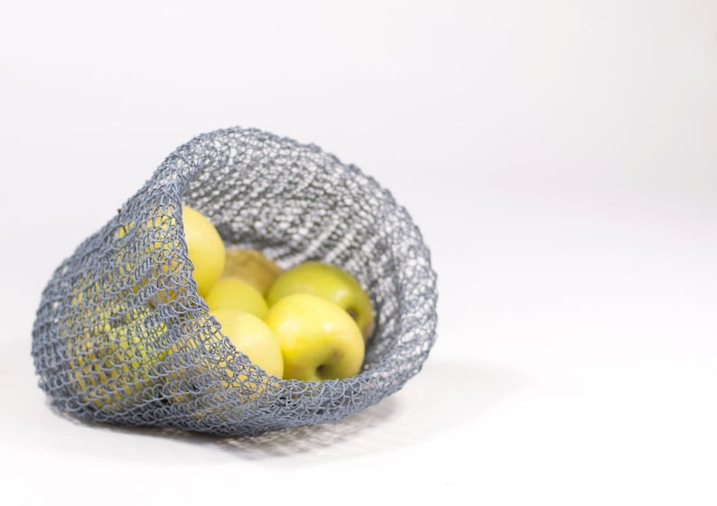 May include: A gray mesh bag filled with yellow apples. The bag is made of a soft, flexible material and is perfect for carrying fruit or vegetables.