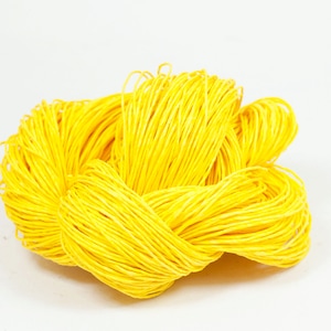 May include: A close-up of a large ball of bright yellow string. The string is tightly wound and appears to be made of a thin, smooth material.