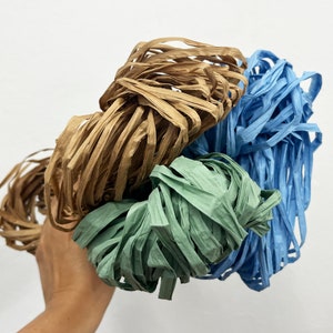 May include: A bundle of three different coloured paper streamers. The streamers are brown, green, and blue. The streamers are curled and twisted together.