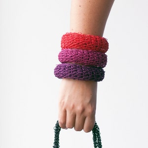 May include: Three crocheted bracelets stacked on a person's wrist. The bracelets are red, pink, and purple.
