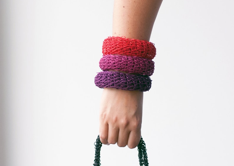 May include: Three crocheted bracelets stacked on a person's wrist. The bracelets are red, pink, and purple.