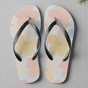May include: A pair of flip-flops featuring a floral design in pastel shades of peach, yellow, and blue. They have black straps and are set against a grey background. The pattern is repeated on both flip-flops.