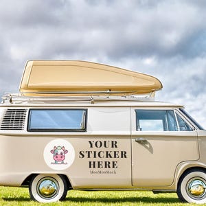May include: A beige and white vintage camper van with a pop-up roof, parked on green grass under a cloudy sky. The van has a round sticker with a cartoon cow and the text "YOUR STICKER HERE".