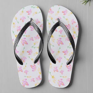May include: White flip-flops featuring a pattern of pink and yellow flowers. The straps are black. These casual flip-flops are ideal for the beach or everyday wear, perfect for warm weather.