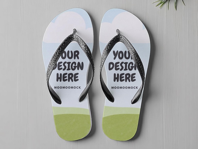 May include: A pair of white flip-flops with black straps. The flip-flops feature a design with a blue sky, clouds, and green grass. The text "OUR DESIGN HERE" and "MOOMOOMOCK" is printed on one flip-flop, and "YOU DESIGN HERE" and "MOOMOOMOCK" on the other.