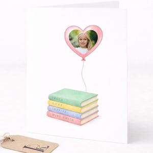 May include: A white greeting card with a pink heart-shaped balloon holding a photo of a child. Below the balloon are four stacked books with the words "Teach, Love, Inspire, Miss Smith." A brown tag with a letter "F" hangs on the left.