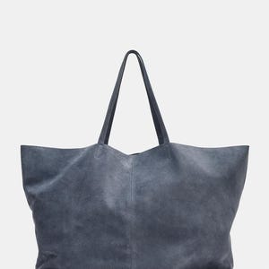 May include: A large, slate blue tote bag with long handles. The bag is made of a soft, suede-like material and has a simple, minimalist design. The handles are attached to the top of the bag and are the same color as the bag.