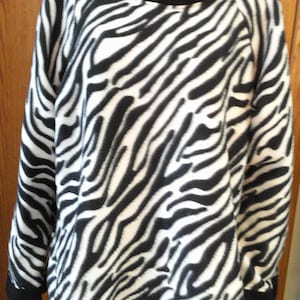May include: A black and white zebra print sweatshirt with a crew neck and long sleeves. The cuffs, neckline, and hem are trimmed with black fabric. The sweatshirt is made of a soft, possibly fleece, material.