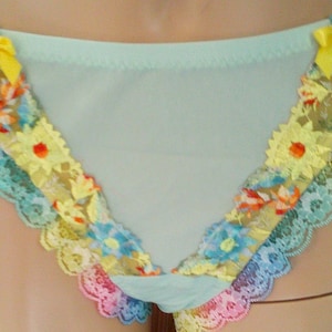 May include: Light blue underwear with floral lace trim in yellow, orange, blue, and pink. The lace is adorned with small yellow bows. The underwear has a soft, delicate appearance.