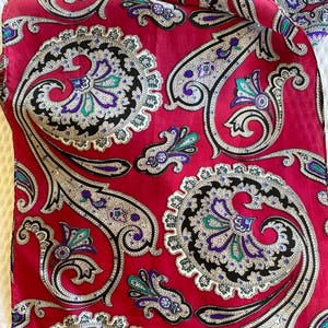 Könnte beinhalten: Ein roter Stoff mit Paisley-Muster und schwarzen, weißen und violetten Akzenten. Der Stoff hat eine glänzende, satinartige Oberfläche.
