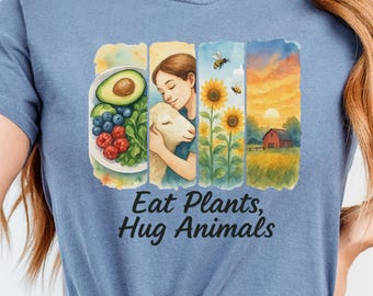 May include: A blue t-shirt with a colorful illustration of a woman hugging a lamb, surrounded by plants, flowers, and a farm scene. The text "Eat Plants, Hug Animals" is printed below the illustration.