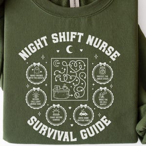 Peut inclure: Sweat-shirt vert militaire avec texte et graphiques blancs. Le texte indique "NIGHT SHIFT NURSE SURVIVAL GUIDE" avec des illustrations d'un labyrinthe, de fantômes et d'une tasse à café. Le sweat-shirt est de style col rond.