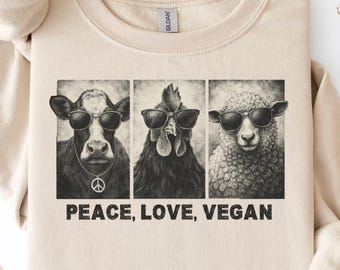 May include: Sand-colored sweatshirt featuring a graphic of a cow, chicken, and sheep wearing sunglasses. The text "PEACE, LOVE, VEGAN" is printed below the images. The sweatshirt has a crew neck and long sleeves.