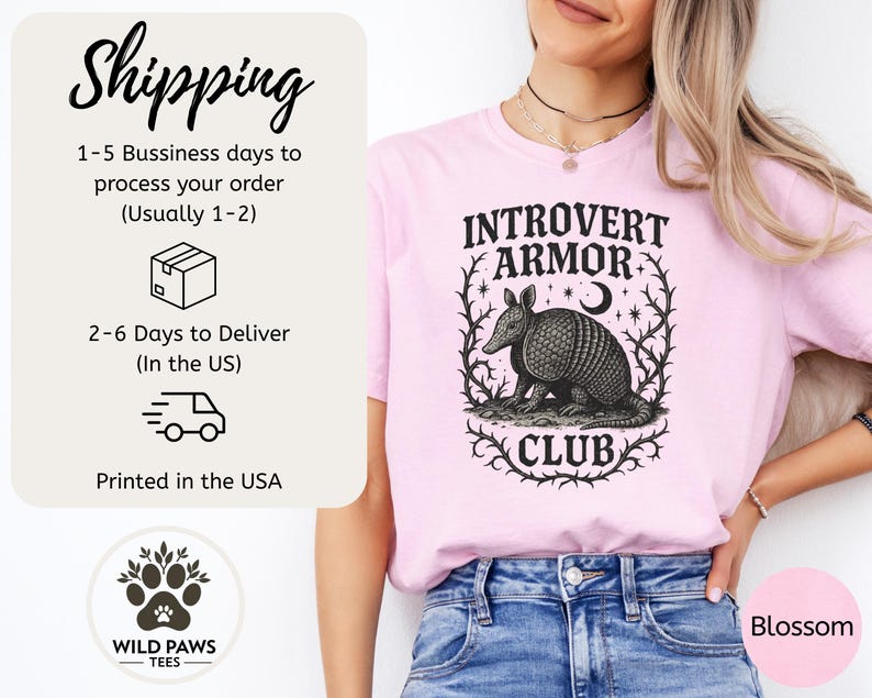 Op de afbeelding: Lichtroze t-shirt met de tekst "INTROVERT ARMOR CLUB" en een gedetailleerde illustratie van een gordeldier. Het shirt is gemaakt van een zacht materiaal en is geschikt voor vrijetijdskleding.