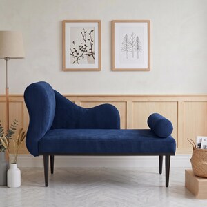 May include: A navy blue chaise lounge with a curved back and a cylindrical armrest. The corduroy-textured upholstery sits on dark wooden legs. Two framed botanical prints hang on the wall behind the lounge.