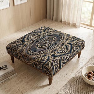 May include: Square ottoman with a dark blue and gold mandala pattern. The ottoman has wooden legs and is placed on a light-coloured tiled floor. A stack of books and a bowl of decorative stones are nearby.
