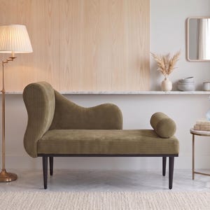 K&ouml;nnte beinhalten: Eine olivgr&uuml;ne Chaiselongue mit geschwungener R&uuml;ckenlehne und Kissenrolle. Eine Messing-Stehlampe mit plissiertem Lampenschirm steht links. Ein kleiner Beistelltisch mit Marmorplatte und ein dekorativer Spiegel befinden sich ebenfalls im Raum.