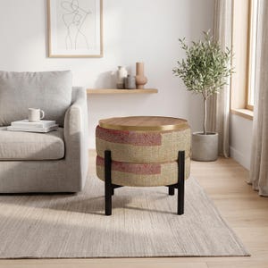 May include: A round ottoman with a textured, woven beige and red fabric body, featuring a smooth wooden top surface with a thin gold-toned metal rim, supported by four straight black legs arranged in a square base configuration.